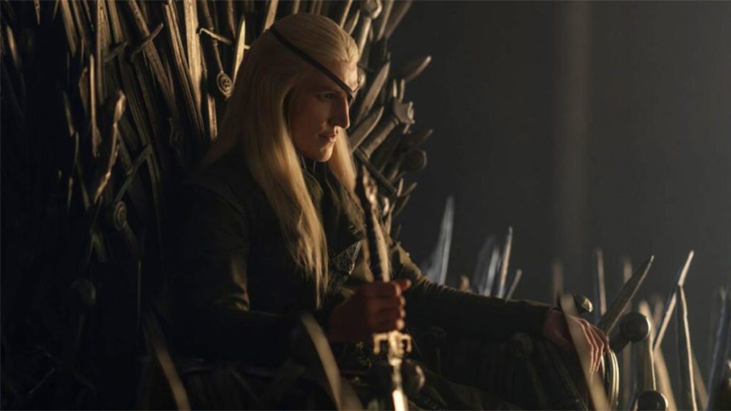 Aemond Targaryen sentado en el trono de espadas usurpado a su hermano, Aegon II Targaryen.