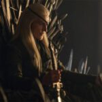 Aemond Targaryen sentado en el trono de espadas usurpado a su hermano, Aegon II Targaryen.